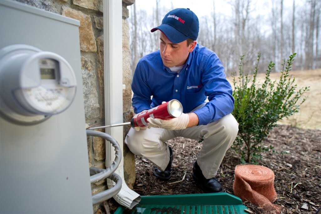 An American Pest technician installing equipment by a home's exterior meter