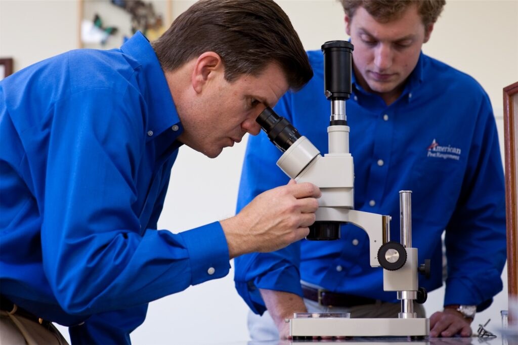 American Pest professionals examining samples under a microscope in the lab