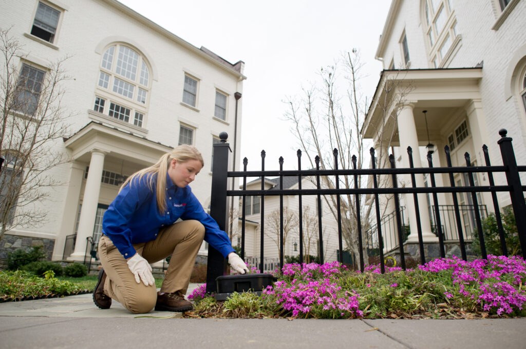 An American Pest technician treating the exterior planting beds of a commercial building
