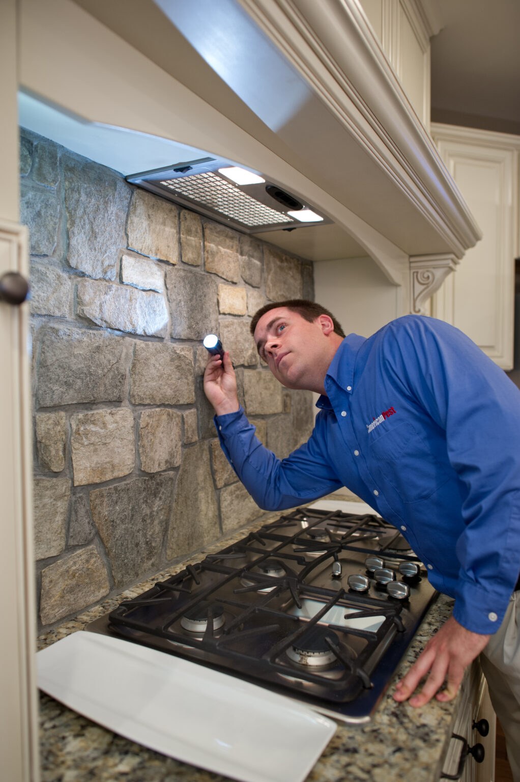 An American Pest technician inspecting a kitchen stove area