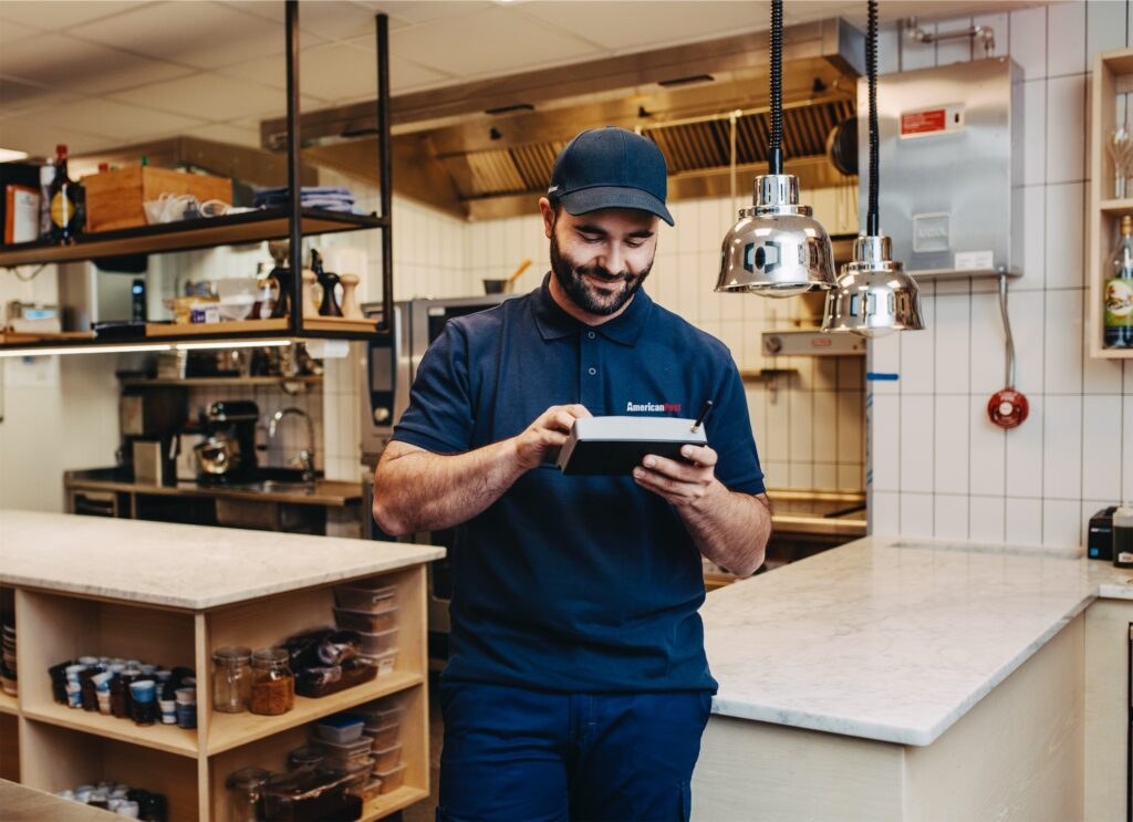 An American Pest technician checking a SMART device reading in a kitchen